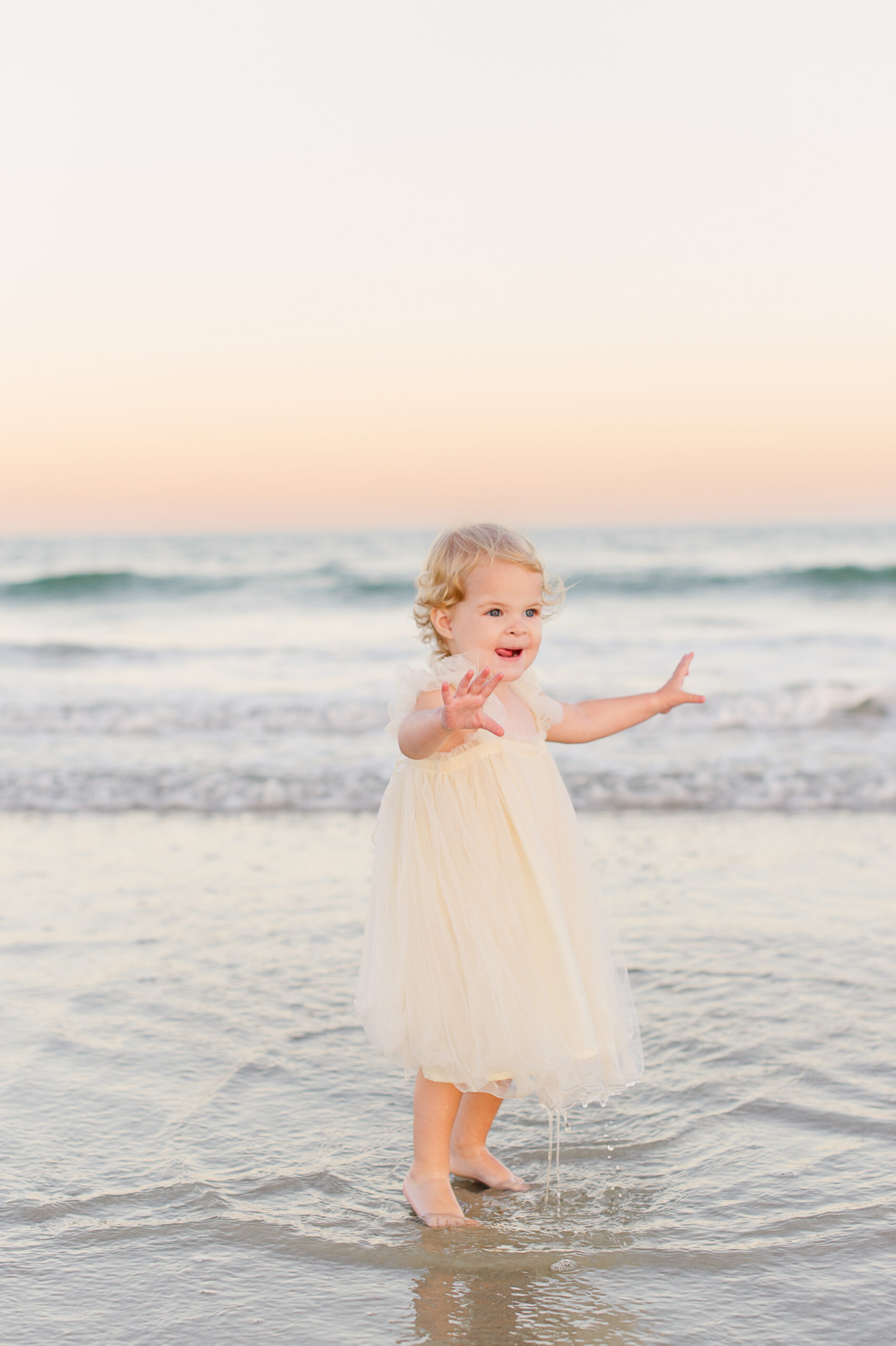 Young toddler girl playing in the water on the beach at the end of their family photography session.