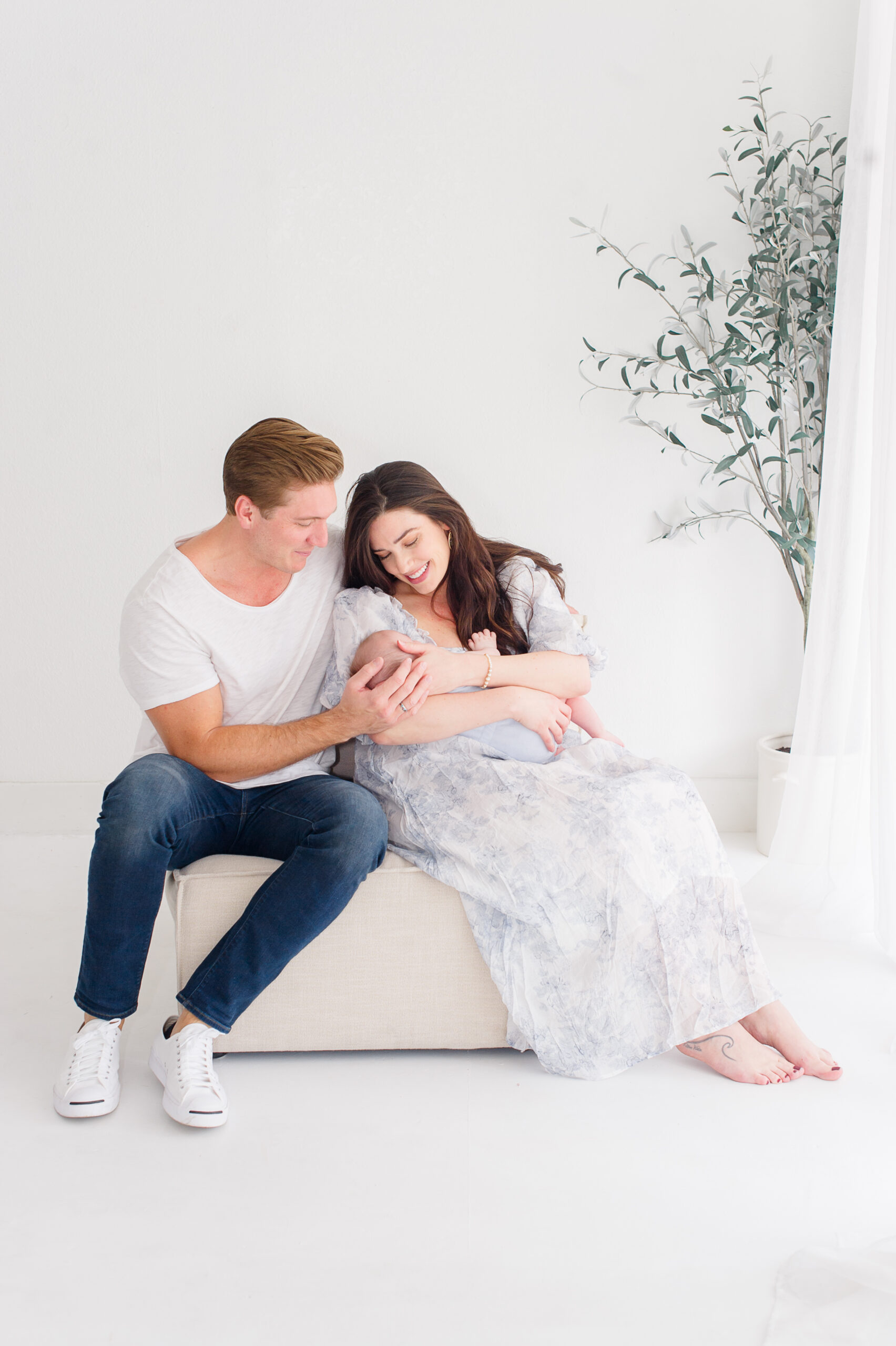 Studio newborn image of a mother and father holding their sweet newborn baby close on a couch in a natural light studio.