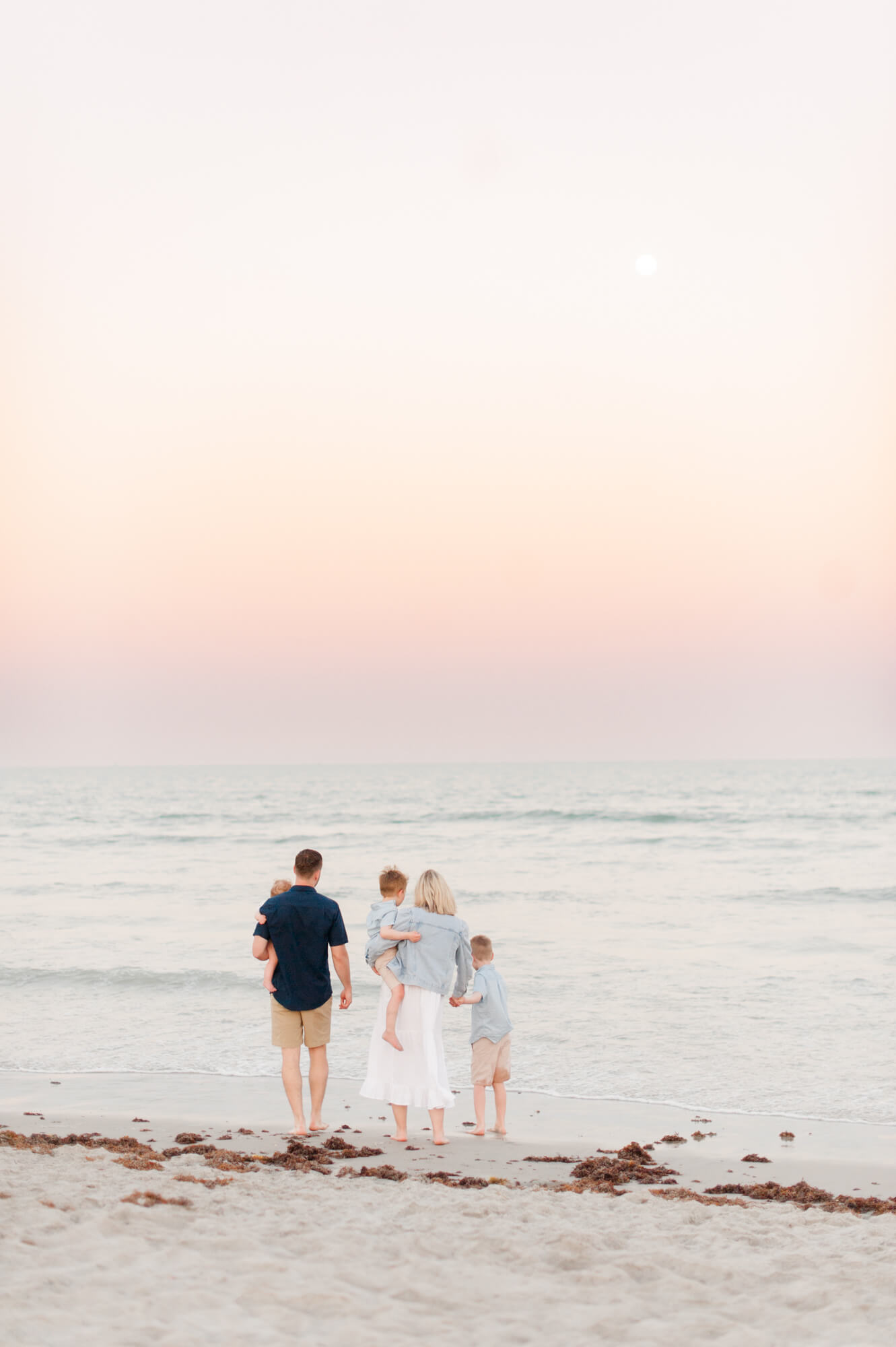 Stunning sunset image of a family of five down by the shore line watching the waves crash during golden hour in Cocoa Beach, Florida Viera Pediatric Dentistry