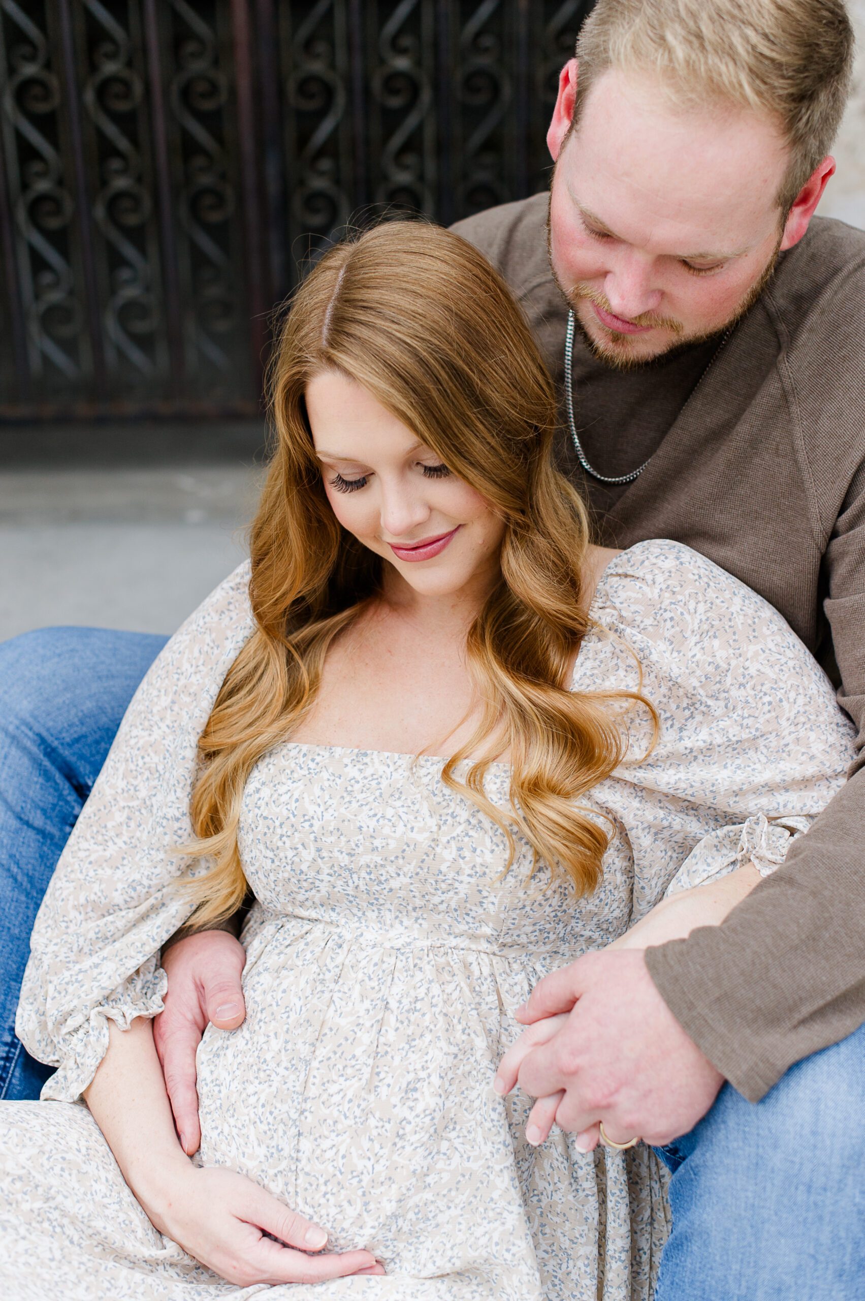 New parents sit on steps and look down toward the mothers pregnant belly during their maternity photoshoot Kissimmee pediatricians