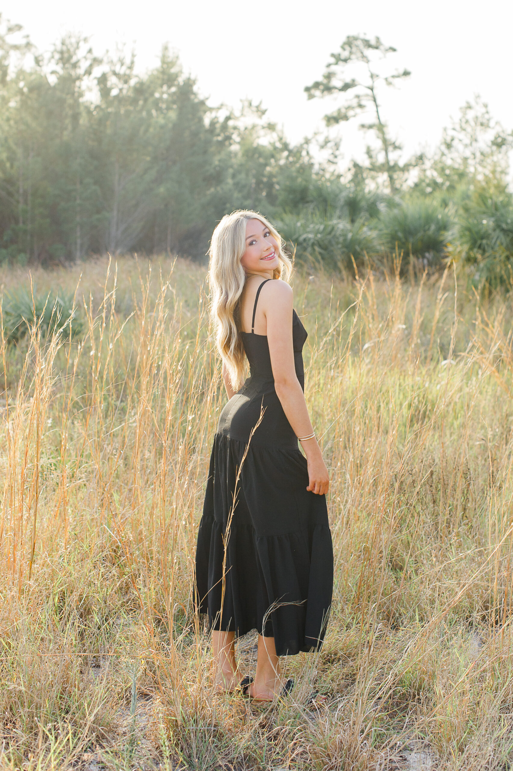 Timber Creek High School senior walking in field of tall grass wearing a black dress during her senior photography session.