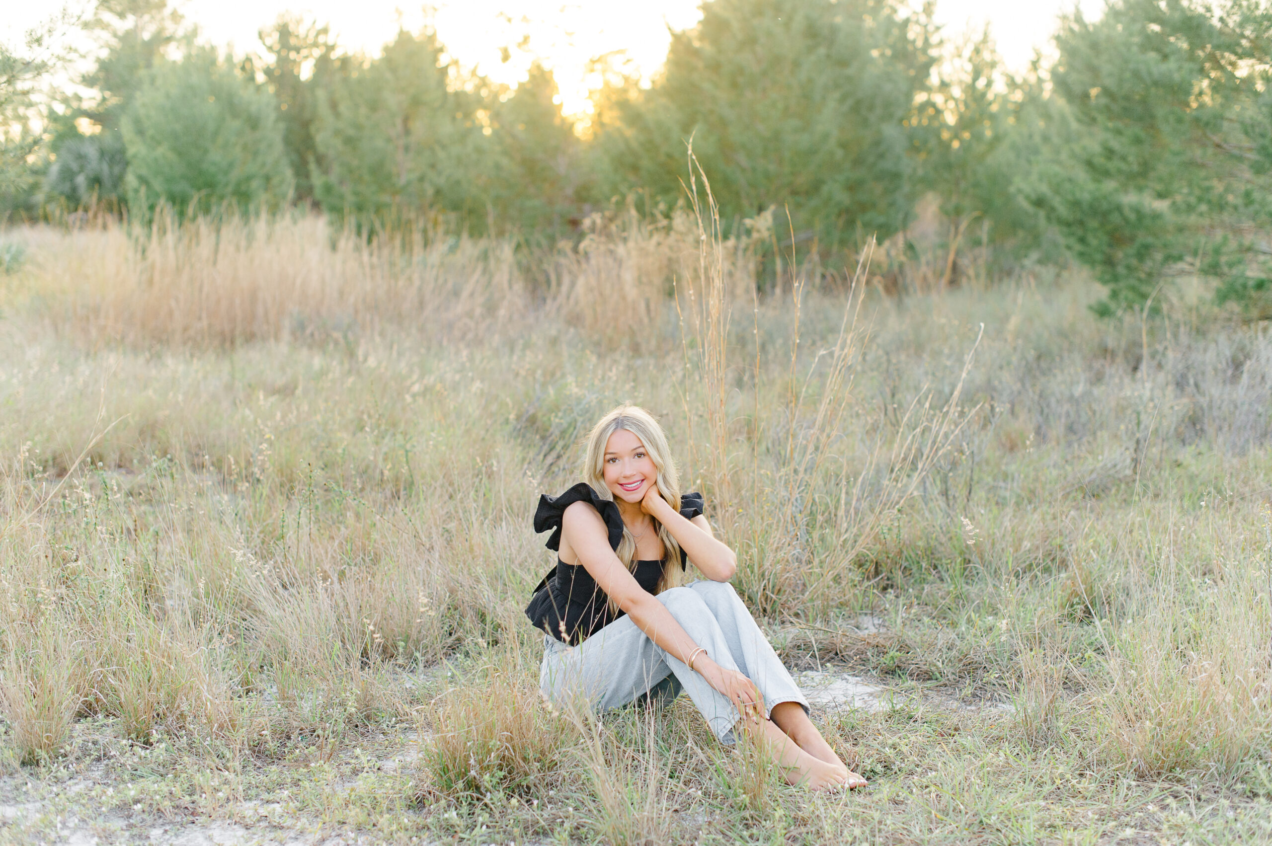 Beautiful blonde Timber Creek High School student sits in a field of tall grass and smiles at the camera during her Senior session with M. Lauren Photography.