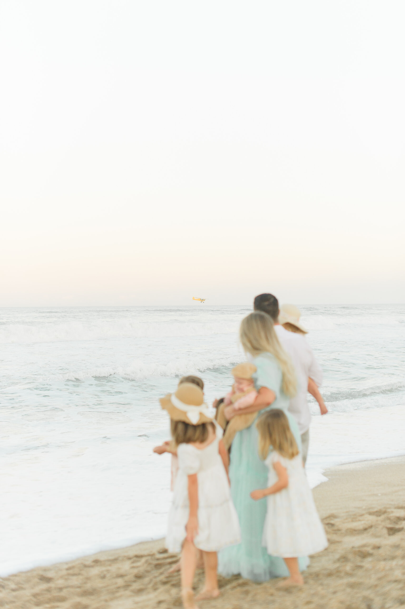 Family watching a plane fly above the ocean during their family session with Daytona Beach Photographer M. Lauren.