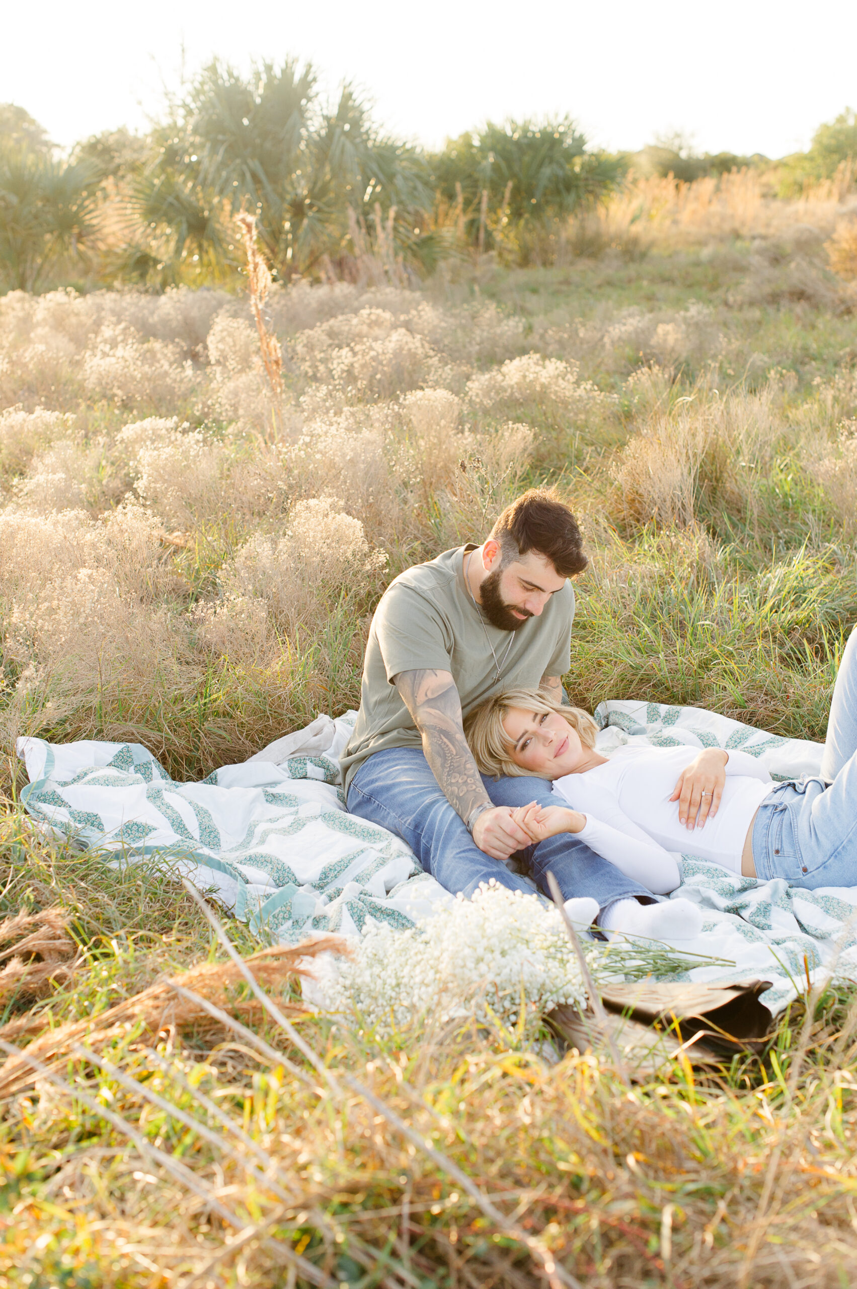 Couple laying in a tall grass field on a blanket given to her by her grandmother celebrating their new engagement with Orlando engagement photographer M. Lauren spas in Orlando