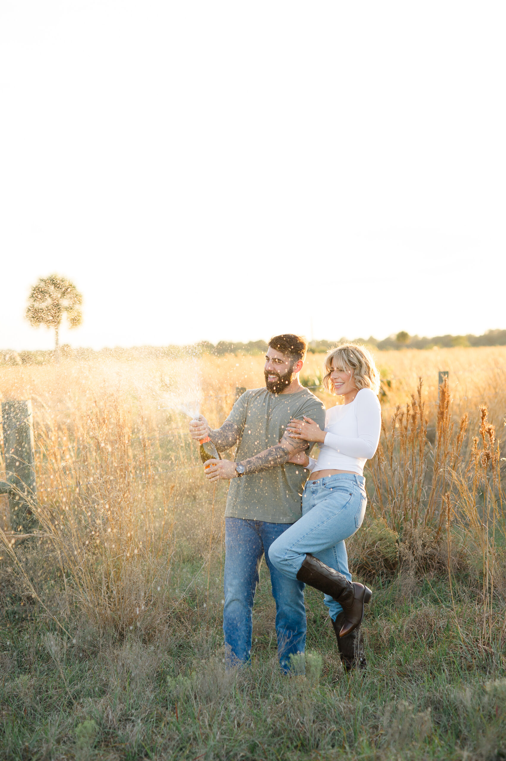 Popping champagne in a tall grass field to celebrate their engagement with orlando couples photographer M. Lauren spas in Orlando