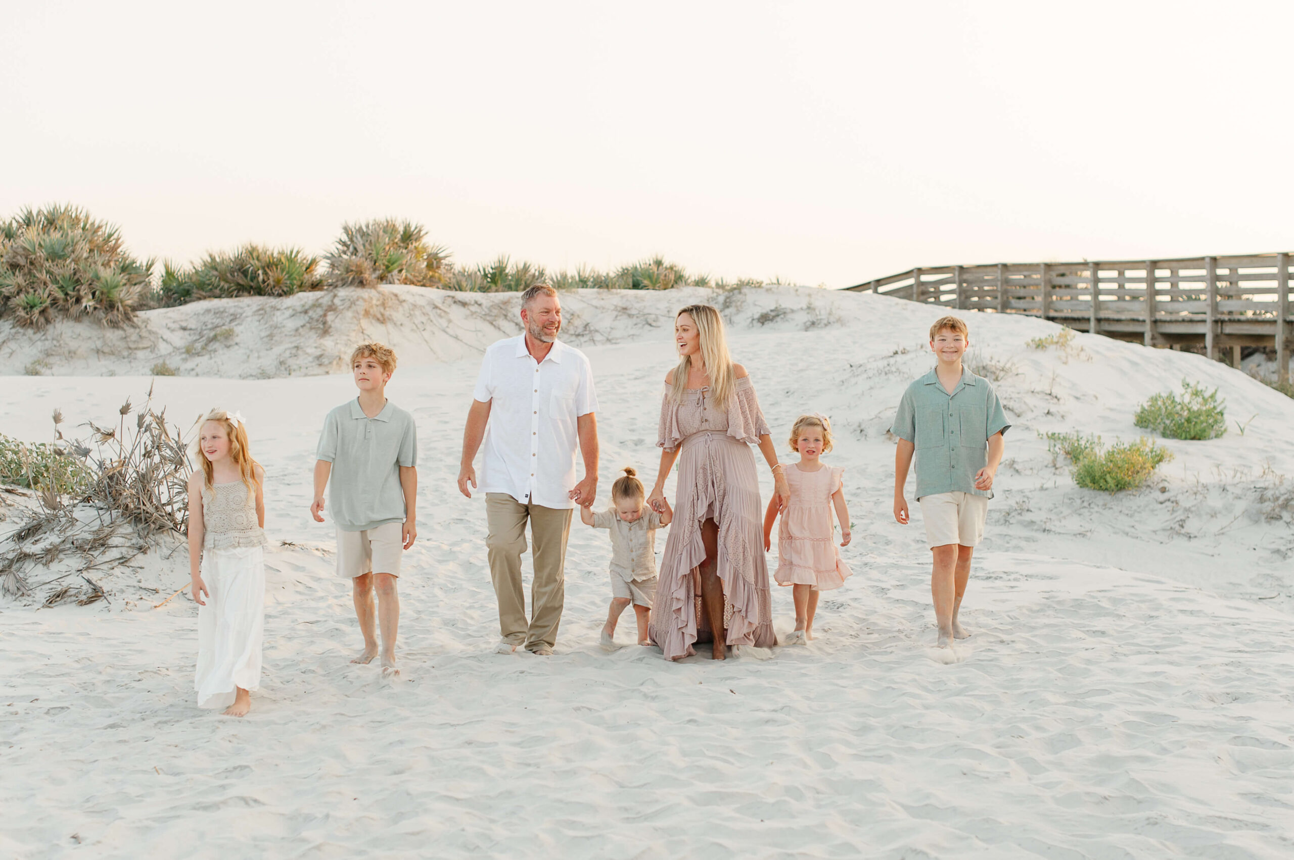 Family of seven walk along the beautiful white sandy dunes in Daytona Beach during their family photography session holding hands.