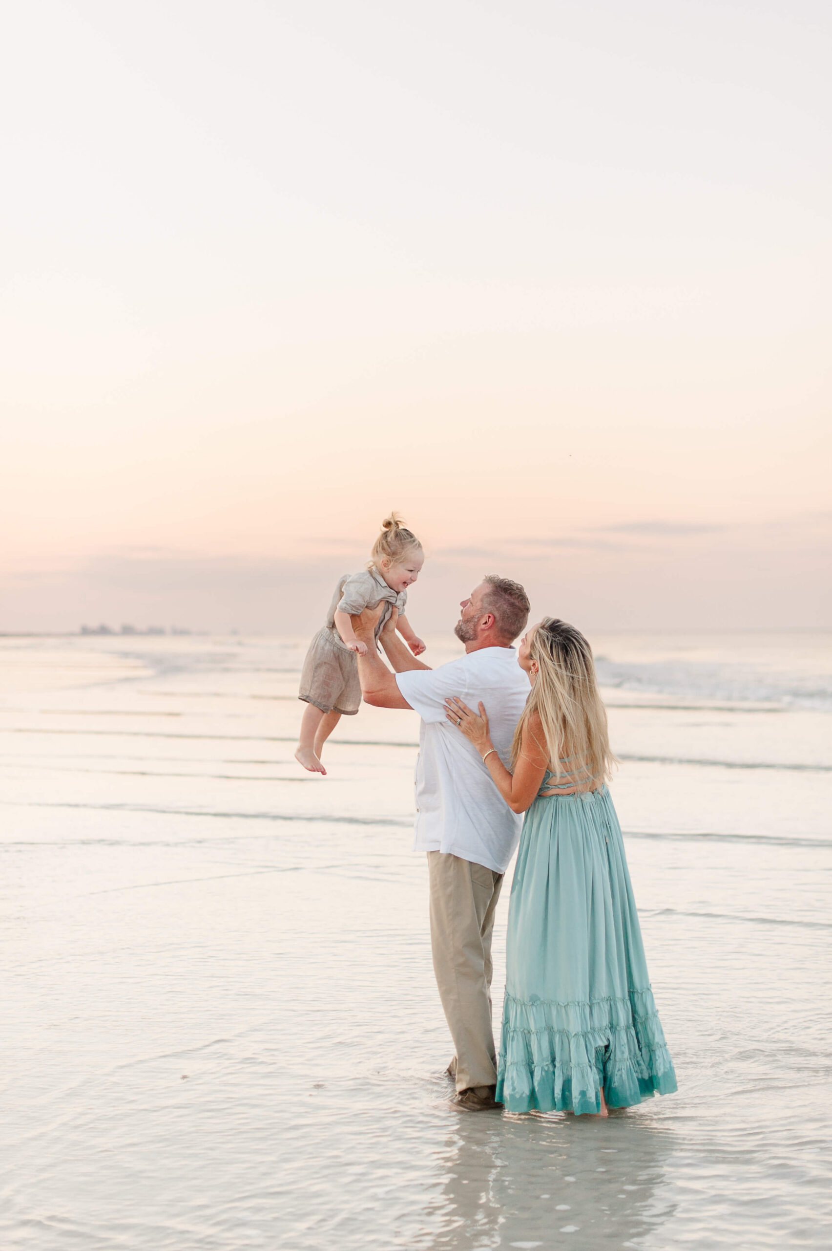Stunning sunset image along the coastline of parents holding their son in the air. 